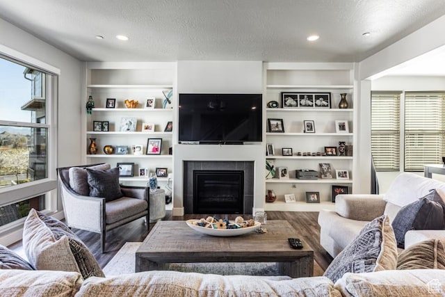 living area featuring a tiled fireplace, wood finished floors, a wealth of natural light, and a textured ceiling