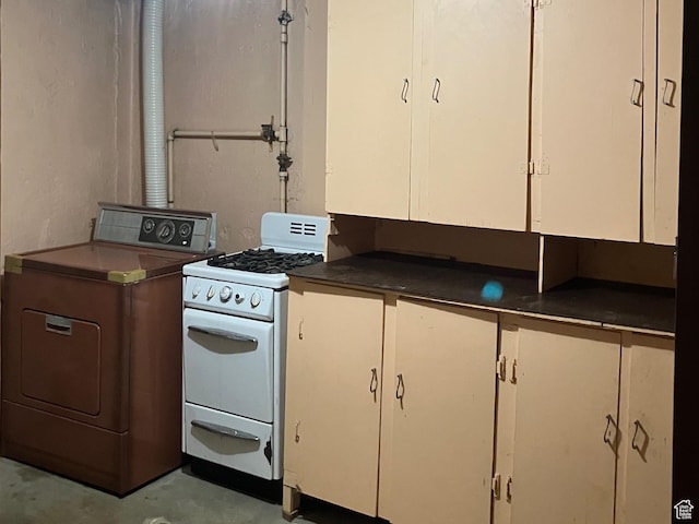 kitchen featuring dark countertops, washer / dryer, concrete floors, white gas range oven, and white cabinetry