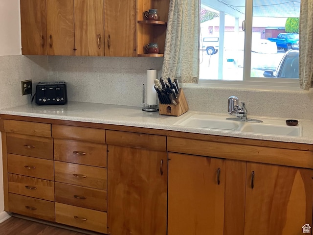 kitchen with tasteful backsplash, open shelves, a sink, brown cabinets, and light countertops