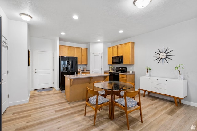 kitchen featuring a center island with sink, light countertops, baseboards, black appliances, and light wood-style flooring