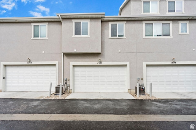 back of property with a garage, central AC unit, and stucco siding