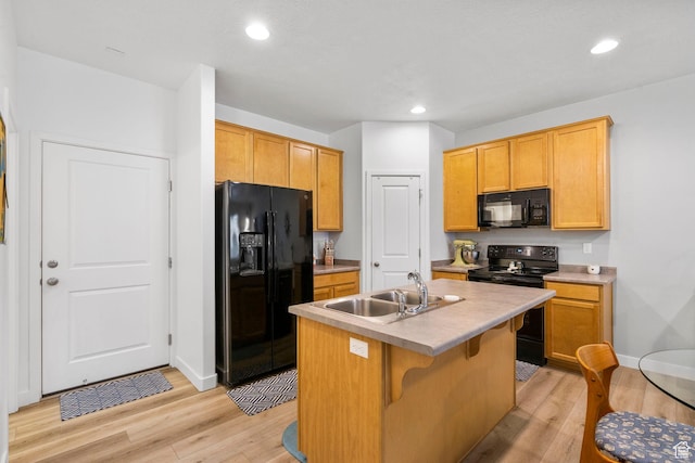 kitchen with a kitchen island with sink, a sink, light countertops, black appliances, and light wood finished floors
