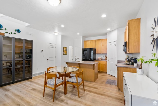 kitchen featuring visible vents, a center island with sink, a sink, light wood-style flooring, and black appliances