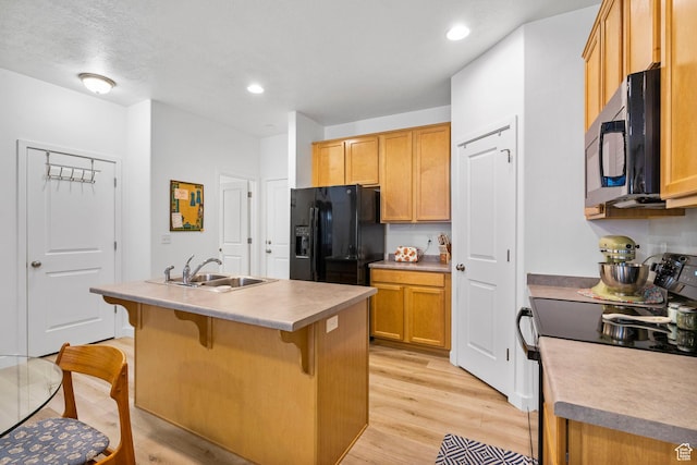 kitchen featuring a sink, light wood finished floors, a kitchen breakfast bar, an island with sink, and black appliances