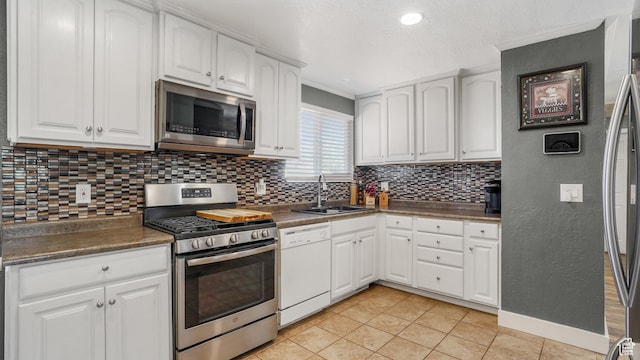 kitchen featuring a sink, tasteful backsplash, dark countertops, white cabinetry, and appliances with stainless steel finishes