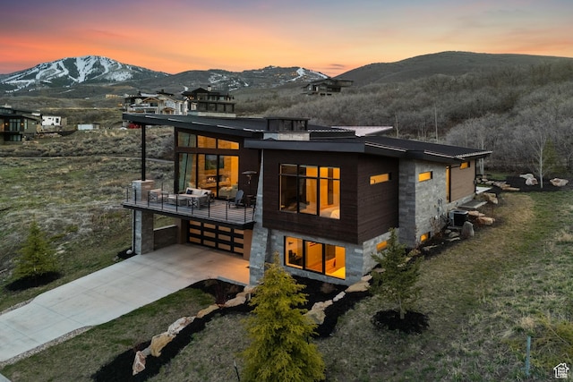 back of property at dusk featuring an attached garage, concrete driveway, a balcony, and a mountain view