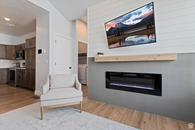 sitting room with washing machine and dryer, light wood-style flooring, a glass covered fireplace, and visible vents