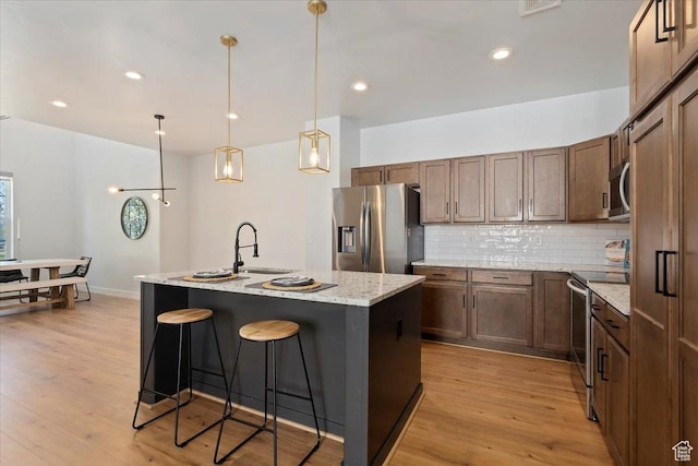 kitchen featuring a kitchen breakfast bar, decorative backsplash, light wood-type flooring, a center island with sink, and appliances with stainless steel finishes
