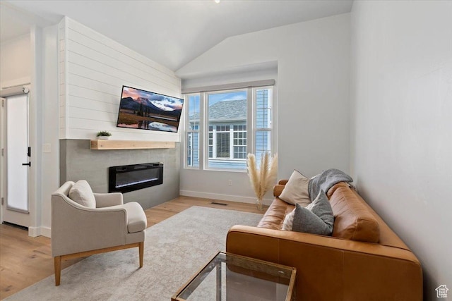 living area featuring wood finished floors, visible vents, vaulted ceiling, baseboards, and a glass covered fireplace