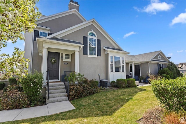 traditional-style house featuring stucco siding, central air condition unit, a chimney, and a front yard