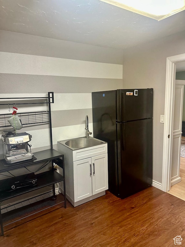 kitchen featuring white cabinets, a sink, baseboards, freestanding refrigerator, and wood finished floors