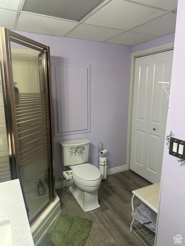 bathroom with wood finished floors, toilet, baseboards, a paneled ceiling, and a stall shower