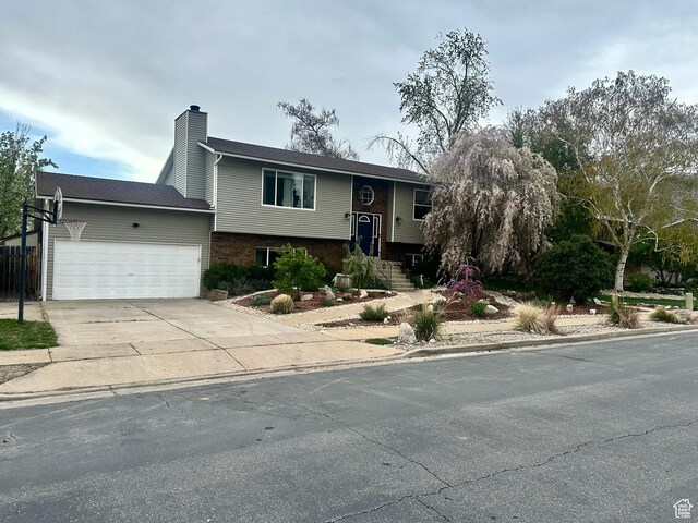 bi-level home featuring an attached garage, driveway, a chimney, and brick siding