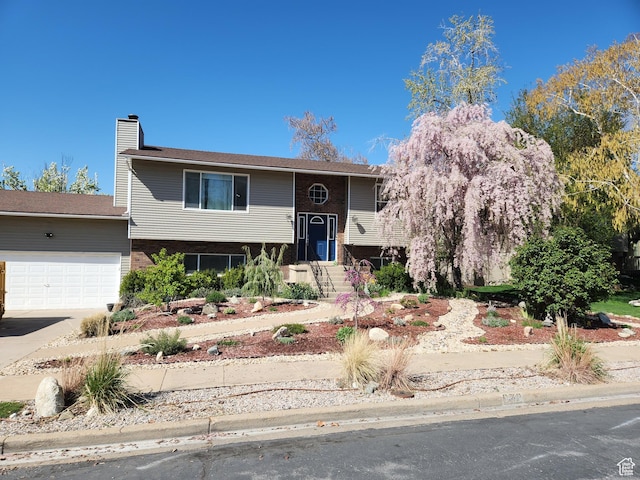 raised ranch with an attached garage, driveway, a chimney, and brick siding
