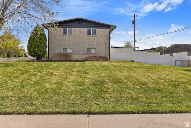 back of property featuring fence, a lawn, and brick siding