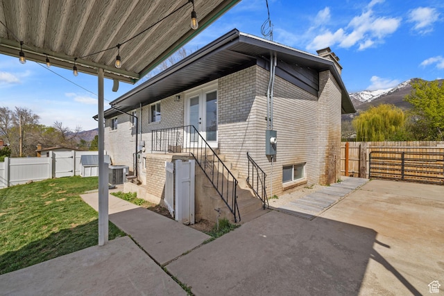 view of front of house featuring a chimney, a fenced backyard, a front lawn, central air condition unit, and a patio area