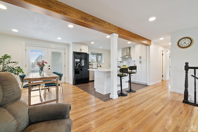 kitchen featuring a kitchen bar, wall chimney range hood, black fridge with ice dispenser, and open floor plan