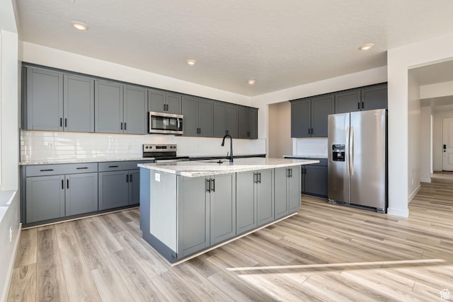 251 E Montgomery Ln, North Ogden, UT 84414 - kitchen featuring a sink, decorative backsplash, light wood-style floors, a center island with sink, and appliances with stainless steel finishes
