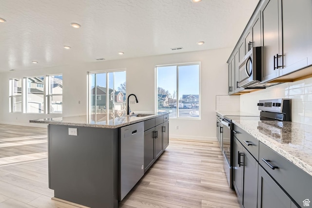251 E Montgomery Ln, North Ogden, UT 84414 - kitchen with a sink, an island with sink, light wood finished floors, appliances with stainless steel finishes, and light stone countertops