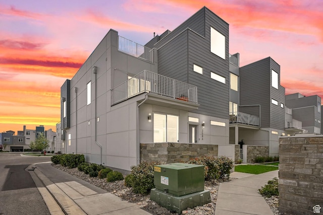 property exterior at dusk featuring stone siding and a balcony
