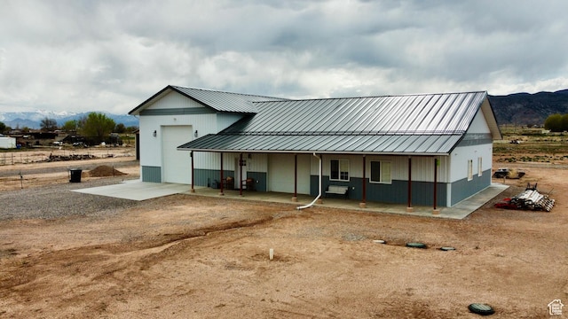 rear view of property with an attached garage, a mountain view, metal roof, and covered porch