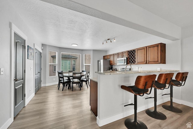 3708 S Luchars Ln W, Salt Lake City, UT 84115 - kitchen featuring a kitchen breakfast bar, light wood-type flooring, baseboards, brown cabinetry, and appliances with stainless steel finishes