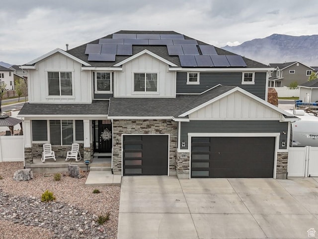 craftsman house featuring a porch, solar panels, fence, concrete driveway, and stone siding