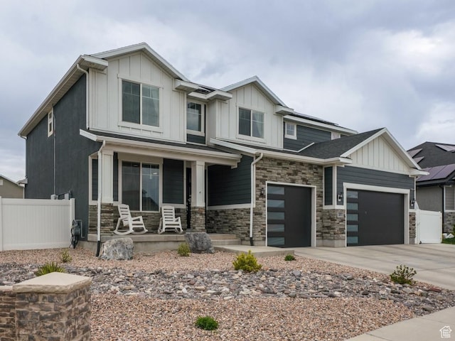craftsman-style house with fence, stone siding, board and batten siding, concrete driveway, and a porch