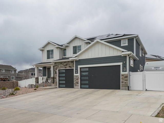 craftsman-style home featuring fence, stone siding, a gate, concrete driveway, and solar panels