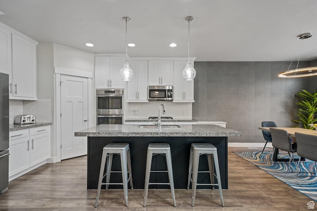 kitchen featuring a kitchen breakfast bar, wood finished floors, a sink, stainless steel appliances, and white cabinetry