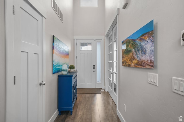 entryway with baseboards, dark wood finished floors, visible vents, and a towering ceiling