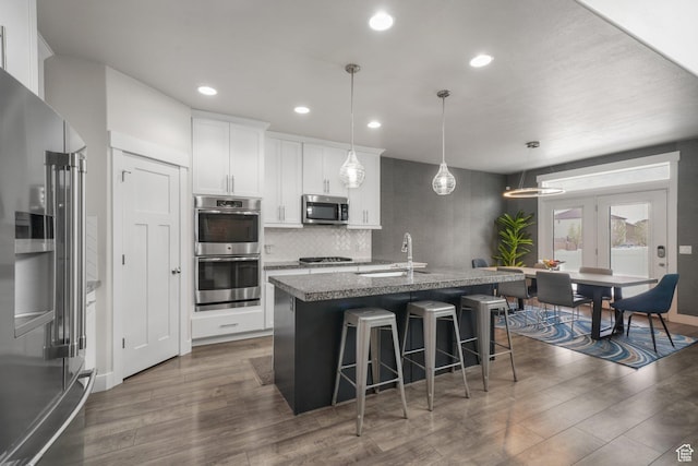 kitchen featuring dark wood-style flooring, a breakfast bar, a center island with sink, a sink, and appliances with stainless steel finishes