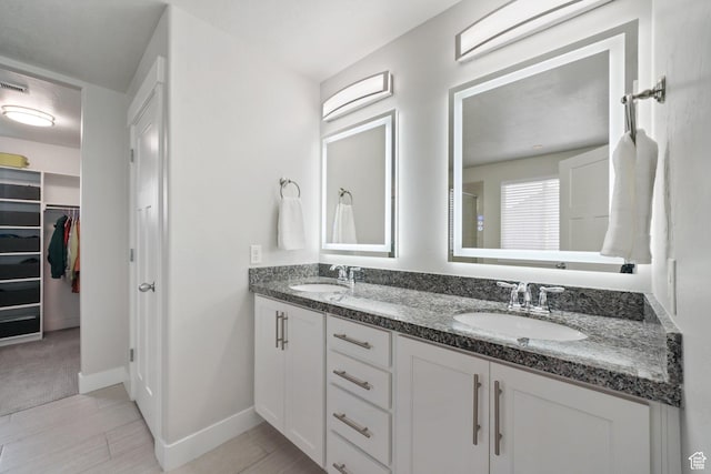 bathroom featuring double vanity, baseboards, a spacious closet, and a sink