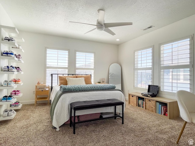carpeted bedroom with a textured ceiling, visible vents, baseboards, and ceiling fan