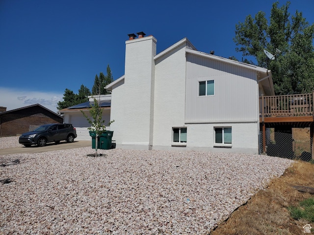 view of property exterior with brick siding, an attached garage, a chimney, and a deck