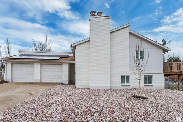 3306 N Fairfield Rd, Layton, UT 84041 - view of home's exterior featuring an attached garage, brick siding, a chimney, concrete driveway, and solar panels