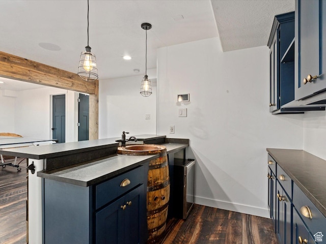 kitchen featuring a peninsula, dark countertops, dark wood-style flooring, and a sink
