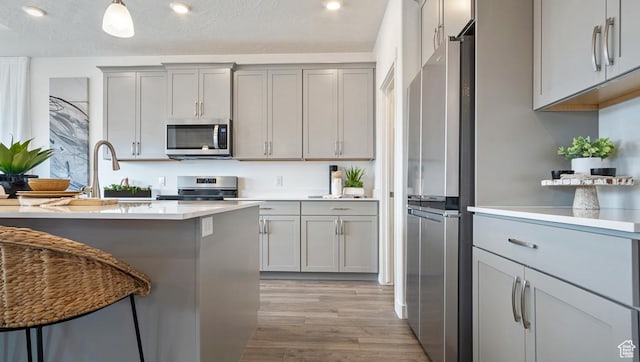 kitchen with stainless steel appliances, recessed lighting, light wood-style floors, gray cabinets, and decorative light fixtures