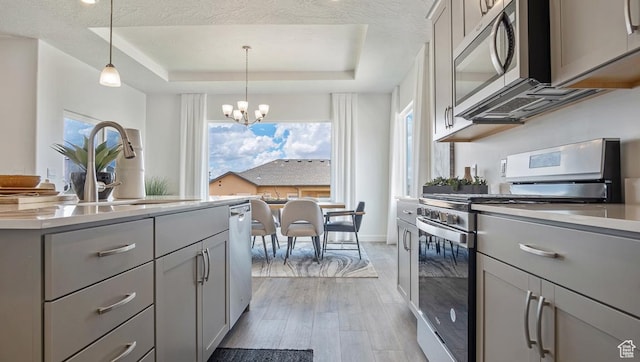 kitchen featuring a sink, light wood-type flooring, a chandelier, gray cabinets, and appliances with stainless steel finishes