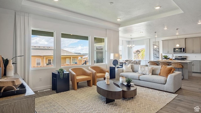 living area featuring light wood-style flooring, a textured ceiling, a chandelier, and a raised ceiling