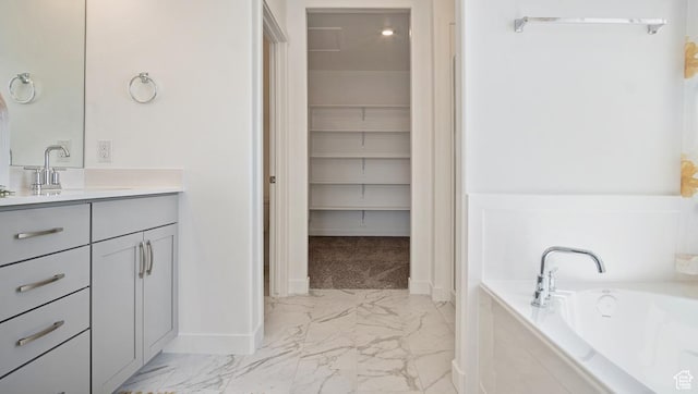bathroom with a garden tub, a walk in closet, vanity, marble finish floor, and baseboards