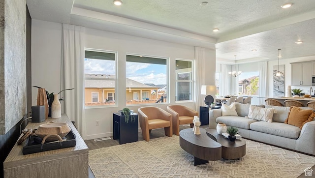 living room featuring a tray ceiling, a textured ceiling, baseboards, an inviting chandelier, and wood finished floors