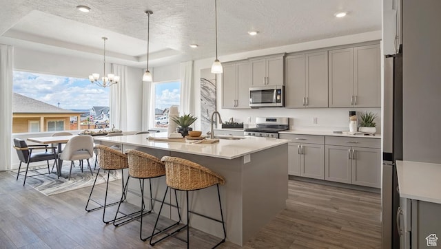 kitchen with a kitchen breakfast bar, a sink, gray cabinets, stainless steel appliances, and dark wood-style flooring