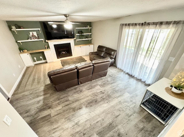 living room with a brick fireplace, wood finished floors, a textured ceiling, and ceiling fan