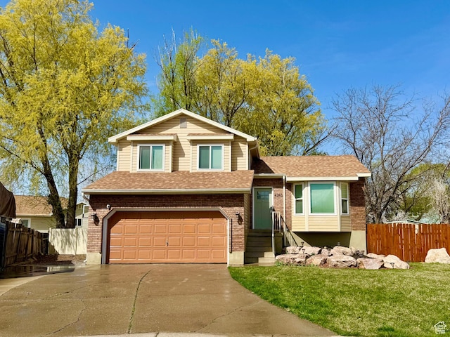 split level home featuring fence, a front lawn, an attached garage, driveway, and brick siding
