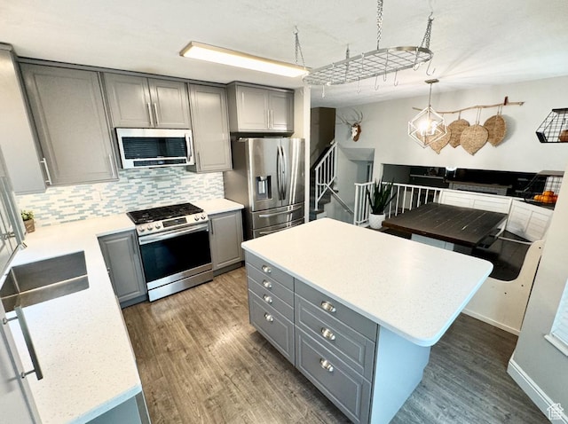 kitchen featuring decorative backsplash, wood finished floors, gray cabinetry, and appliances with stainless steel finishes