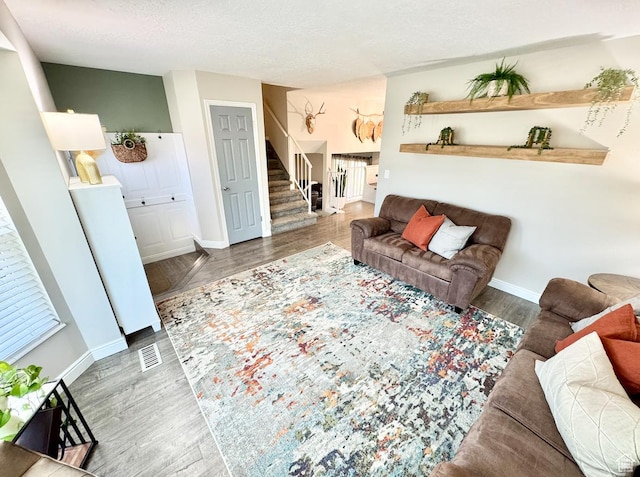living area with stairway, wood finished floors, visible vents, baseboards, and a textured ceiling