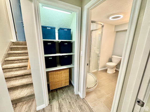 interior space with baseboards, a textured ceiling, toilet, and a stall shower