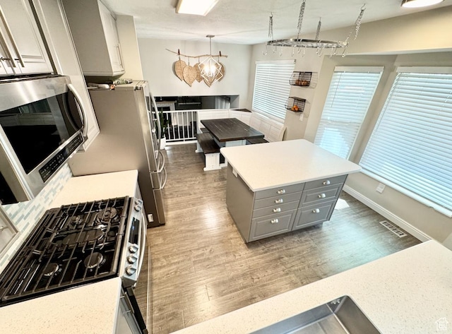 kitchen featuring light countertops, gray cabinets, light wood-type flooring, a kitchen island, and appliances with stainless steel finishes