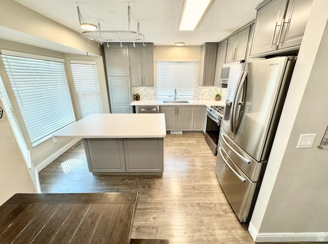 kitchen featuring light wood finished floors, stainless steel appliances, a sink, decorative backsplash, and gray cabinetry